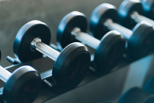 Dumbbell rack with black weight plates and metal handles in modern gym, creating focused fitness training atmosphere with orderly equipment and cool blue lighting