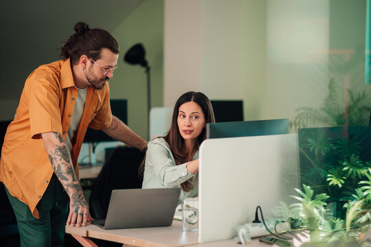 Colleagues collaborating on a desktop computer, analyzing data and discussing ideas in a contemporary workspace