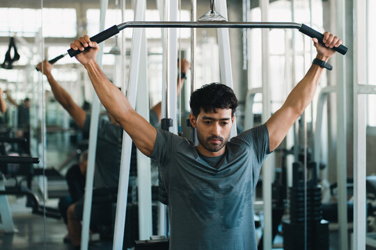 Man performing lat pulldown exercise in modern gym with focused expression and strength training equipment