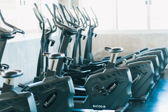 Indoor fitness studio with stationary bicycle and elliptical machine arranged in rows near bright windows, creating clean modern workout environment with cool blue tones