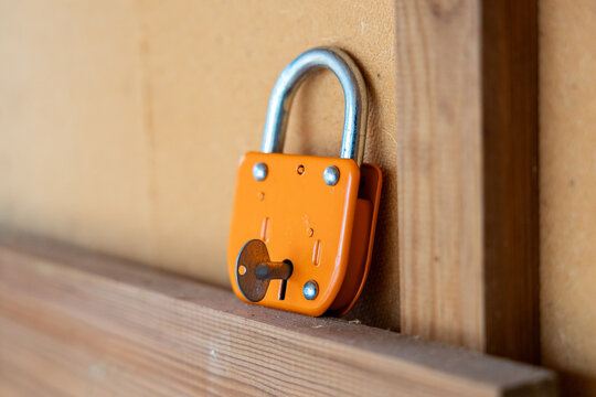 Orange padlock with rusty key rests on a wooden frame, providing concept of security, access, safety, defense, privacy, protection, and mechanical hardware.