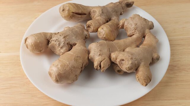 Fresh ginger roots rotating on a white plate
