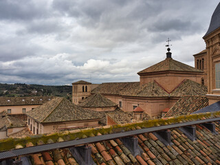 Old City Rooftops Under Cloudy Sky - An elevated view over the historic rooftops of a Spanish city, showcasing terracotta tiles, brick buildings, and a distant green landscape u © jmag.foto