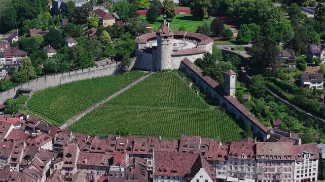 Aerial orbital tracking view of the historic Munot fortress and its green vineyard, overlooking the old town roofs in Schaffhausen, Switzerland.