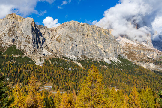 An autumn landscape with golden larches and surrounding mountains on a sunny day with a blue sky near Passo Pordoi in the Dolomites.