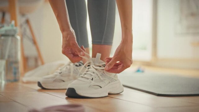 In snug home gym, focused athlete laces her white sneakers, prepping for personal fitness training session. The intimate setting highlights individual workout routines in comfortable, familiar space