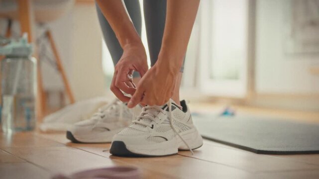 Inside her kitchen, young athlete carefully ties the laces of her white sneakers, prepping for a home training session that highlights a proactive, gym-free fitness routine, while sunlight streams in