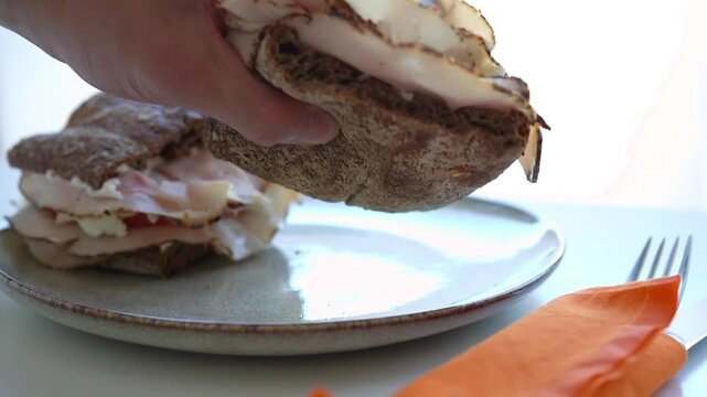 Man's hand taking a deli style turkey pastrami sandwich to eat