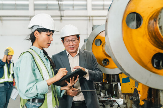 Factory engineer inspecting industrial machine with senior supervisor during workplace discussion