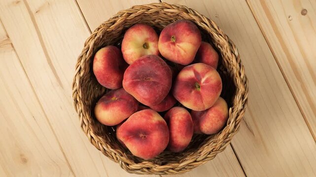 Wicker basket of ripe flat peaches rotating on a wooden table
