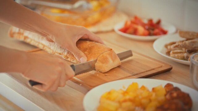 Slicing fresh bread. A housewife uses a serrated bread knife on a wooden cutting board in the home kitchen. The concept of healthy home cooking and everyday culinary practices