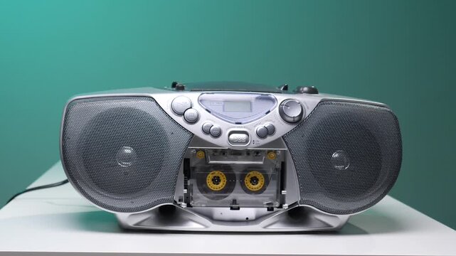 Hand pressing a button on a silver boombox with a cassette tape inserted, symbolizing vintage audio technology, music playback, and a nostalgic experience from past decades