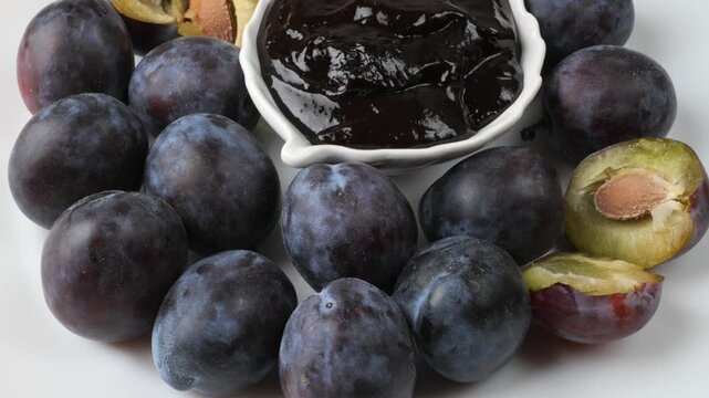 Fresh plums and delicious jam rotating on white background