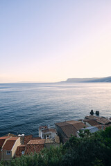 Scenic view of Scilla in Calabria, Italy, with traditional red rooftops overlooking calm Mediterranean water under a soft pastel morning sky, ideal for travel and destination themes. © Jacek