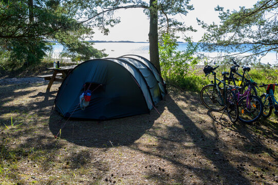 A tent and bicycles set up at a lakeside campsite in Nyk&ouml;ping, Sweden during a warm summer sunrise.