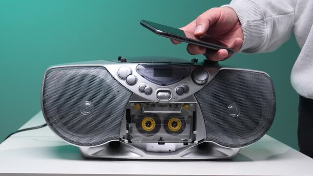 Hand holding a modern smartphone over a vintage boombox with a visible cassette tape, symbolizing the evolution of music technology and the blend of analog and digital eras