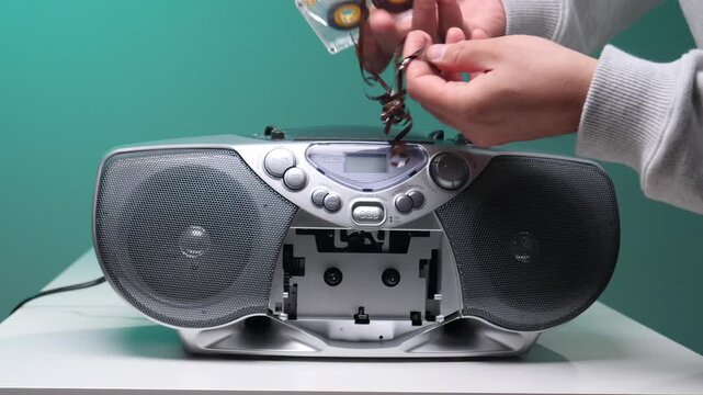 Hands extracting a tangled magnetic tape from a damaged audio cassette stuck in an old boombox, symbolizing audio technology nostalgia, malfunction, and repair challenges