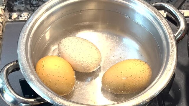 Close-up of three eggs starting to boil in a pot of water on a stove with tiny bubbles forming.