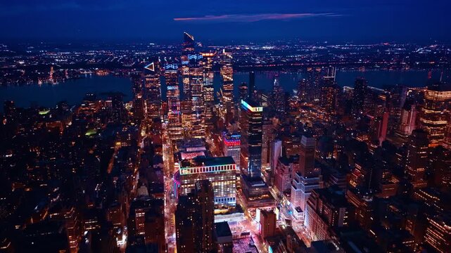 Beautifully illuminated Hudson Yards neighborhood at night. Drone flight above the gorgeous scenery of New York City, USA at the river waterfront.