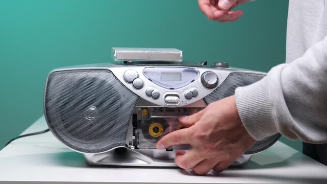 Hand pressing play button on an old fashioned silver cassette player, enjoying vintage audio music with a tape inserted, showing retro technology and sound