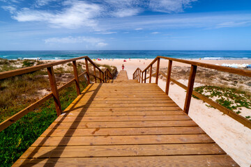 Obraz premium Wooden boardwalk to Praia de Paredes da Vitória beach with people, Atlantic Ocean, holiday background, Portugal, Nazaré, Leiria.