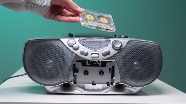 Hand inserting an old transparent audio cassette tape into a classic silver boombox player, evoking a feeling of nostalgia for analog music and vintage technology