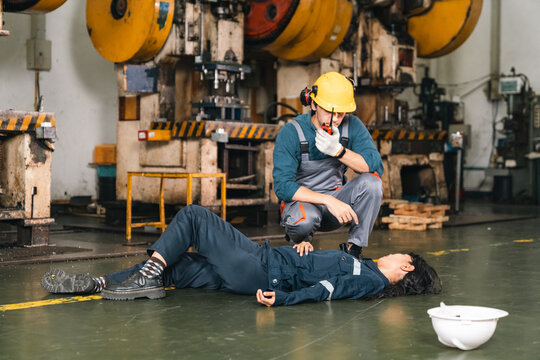 Industrial worker assisting injured colleague on factory floor with safety equipment and machinery