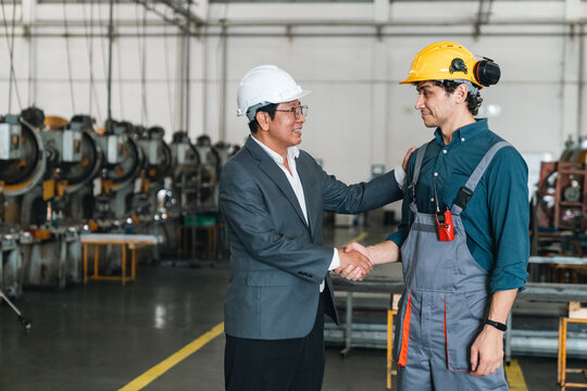 Industrial manager and technician shake hands inside factory, showing teamwork, trust, and professional collaboration during workplace meeting in manufacturing facility