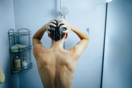 Athletic man applying shampoo to his wet head during a hot shower.
