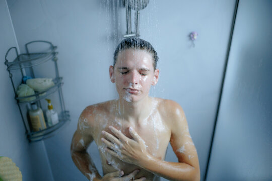Relaxed teenager with eyes closed standing under falling shower water.