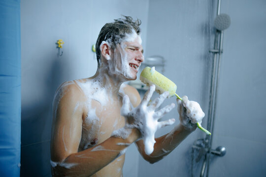 Joyful teenager singing with a bath sponge microphone during morning shower.