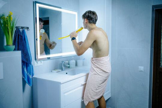 Energetic teen boy singing into yellow bath brush standing inside the bathroom.