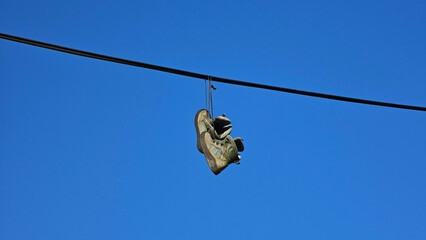 Obraz premium Pair of worn sneakers hanging by their laces over an overhead utility cable against a clear blue sky background