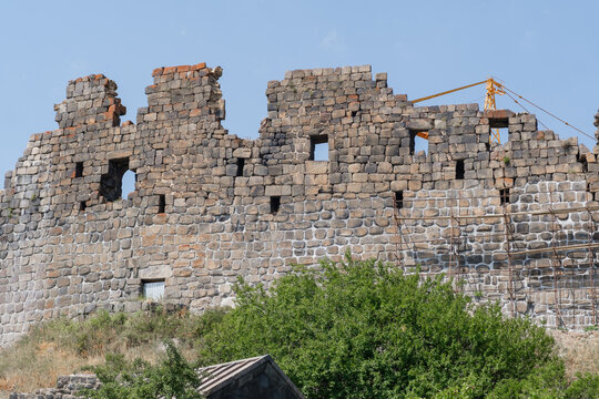 Amberd Fortress features weathered stone walls with openings, surrounded by lush greenery under a clear blue sky, representing historical architecture