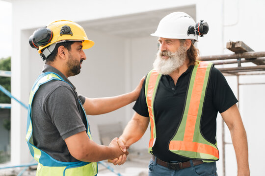Two construction worker wearing safety helmet and reflective vest shake hand at building site, showing teamwork, trust, and professional cooperation during successful workday