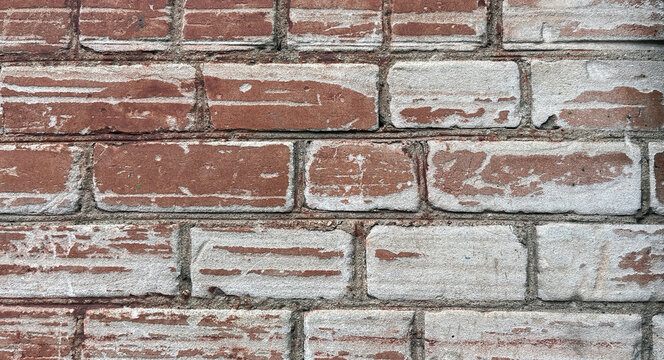 Close‑up of a weathered brick wall with remnants of white paint or limewash, showcasing aged masonry, rough mortar joints, and a rustic architectural texture with contrasting red and white tones.