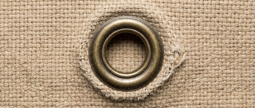 Brass metal grommet eyelet on beige canvas fabric. Macro shot of woven textile hole
