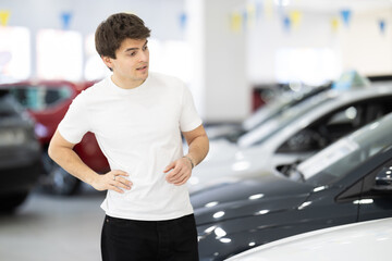 Young male buyer choosing and examines new cars in modern car dealership © JackF