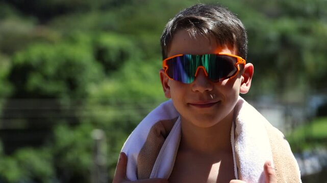 Boy wearing sunglasses preparing to swim outdoors looks towards camera and smirks - isolated shot