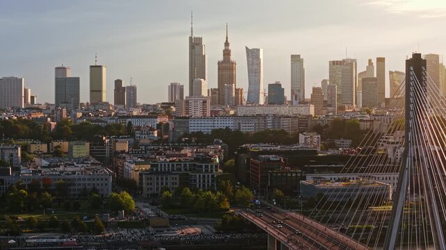 Rising drone establishing aerial shot of Warsaw skyline at golden hour, with modern skyscrapers, city center, Vistula River and cable-stayed bridge in cinematic view