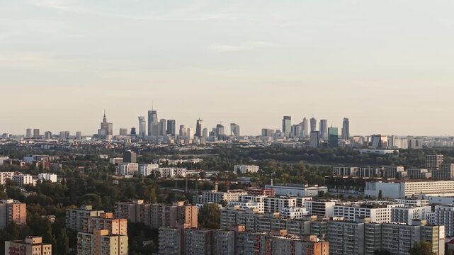 Smooth aerial drone panorama across Warsaw, revealing expansive cityscape with modern downtown skyline, skyscrapers, residential districts, green urban areas and dense architecture in evening light