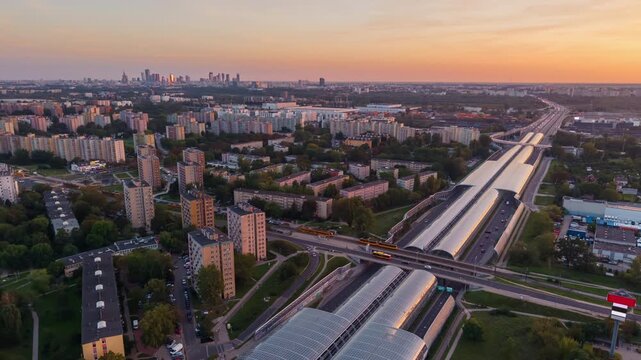 Static aerial drone timelapse of Warsaw S8 expressway at sunset, with traffic flowing through glass acoustic tunnels, residential districts and distant downtown skyline under warm evening sky