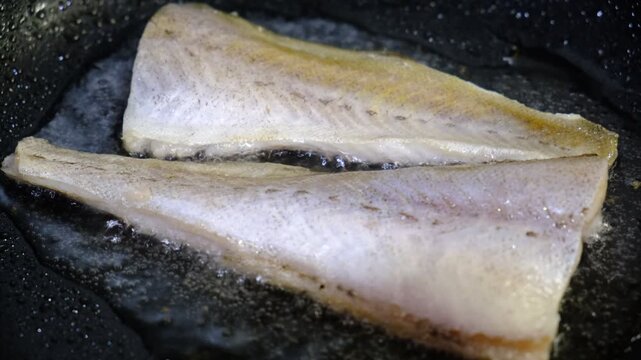 Indoor cooking scene: seasoned cod fillets are pan‑grilled in a cast‑iron skillet on a stovetop. Sizzle and texture of the fish as it cooks, highlighting the golden sear and aromatic seasoning.
