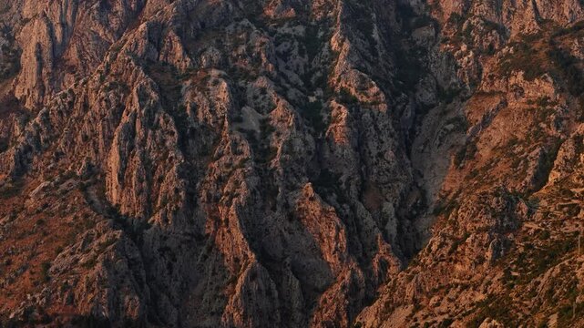 montenegro - aerial tracking view along a steep rocky cliff face with deep shadowed gullies in low warm evening sun, a moody b roll background with copy space in the dark areas
