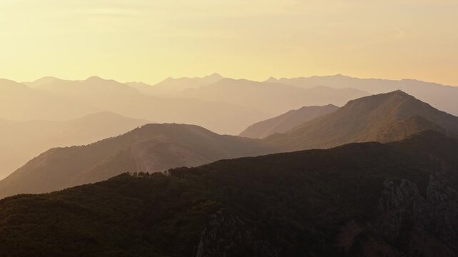 aerial drift above a forested mountain ridge at sunset with range after range of hills fading into golden haze, a calm moody b roll shot for titles and transitions, montenegro