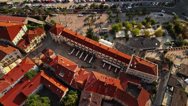 kotor, montenegro - aerial top down view of the main square of kotor old town with its stone clock tower, market canopies, cafe seating and the palm lined promenade beyond