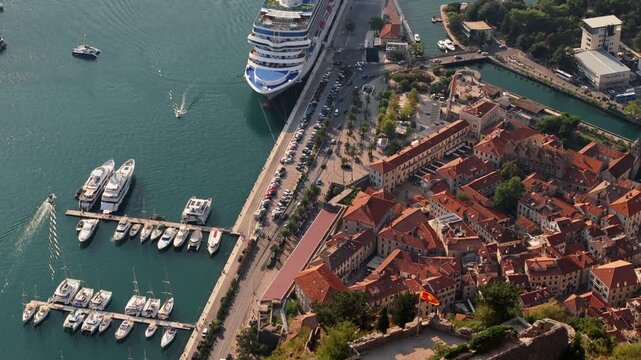 kotor, montenegro - aerial tracking view along the kotor waterfront promenade with parked cars, palm trees, yacht berths and a cruise ship at the quay in warm afternoon light