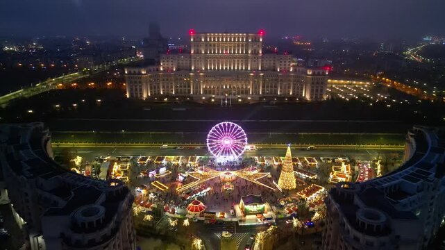 Aerial drone footage of the festive Bucharest Christmas Market illuminated at night in Constitution Square (Piata Constitutiei), featuring the glowing Ferris wheel, decorated Christmas tree.