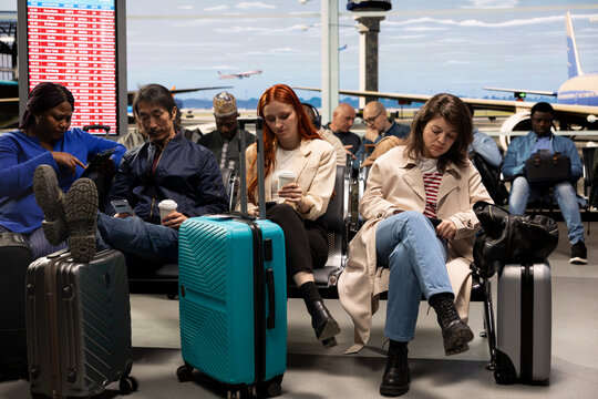 Multiethnic men and women use a mobile phone at the airport to text about arriving home late after a delayed flight, checking schedule status and travel disruption during international travel.
