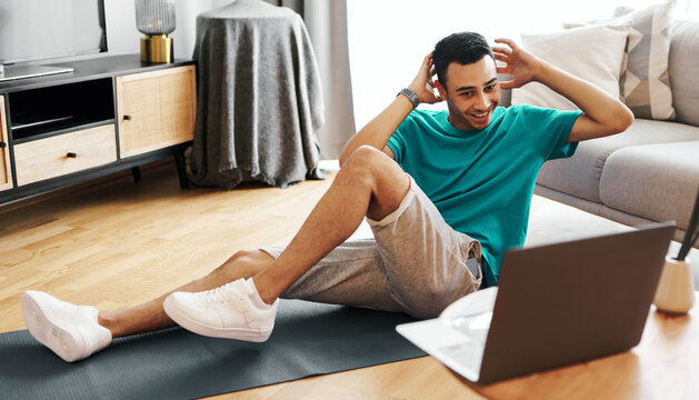 Happy Young Hispanic Male Doing Exercises While Working Out At Home On Mat, Focusing On His Fitness Routine In Modern Living Room, Engaged In Healthy Lifestyle.